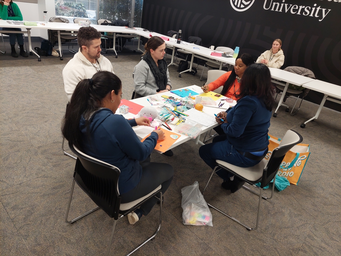 Five students sitting around a table participating in a group work activity with coloured pencils and paper.