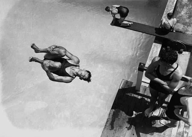 Man diving into pool with other divers waiting and watching